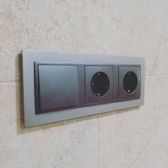 Interruptor y enchufes modernos con marco de aluminio instalados en una pared